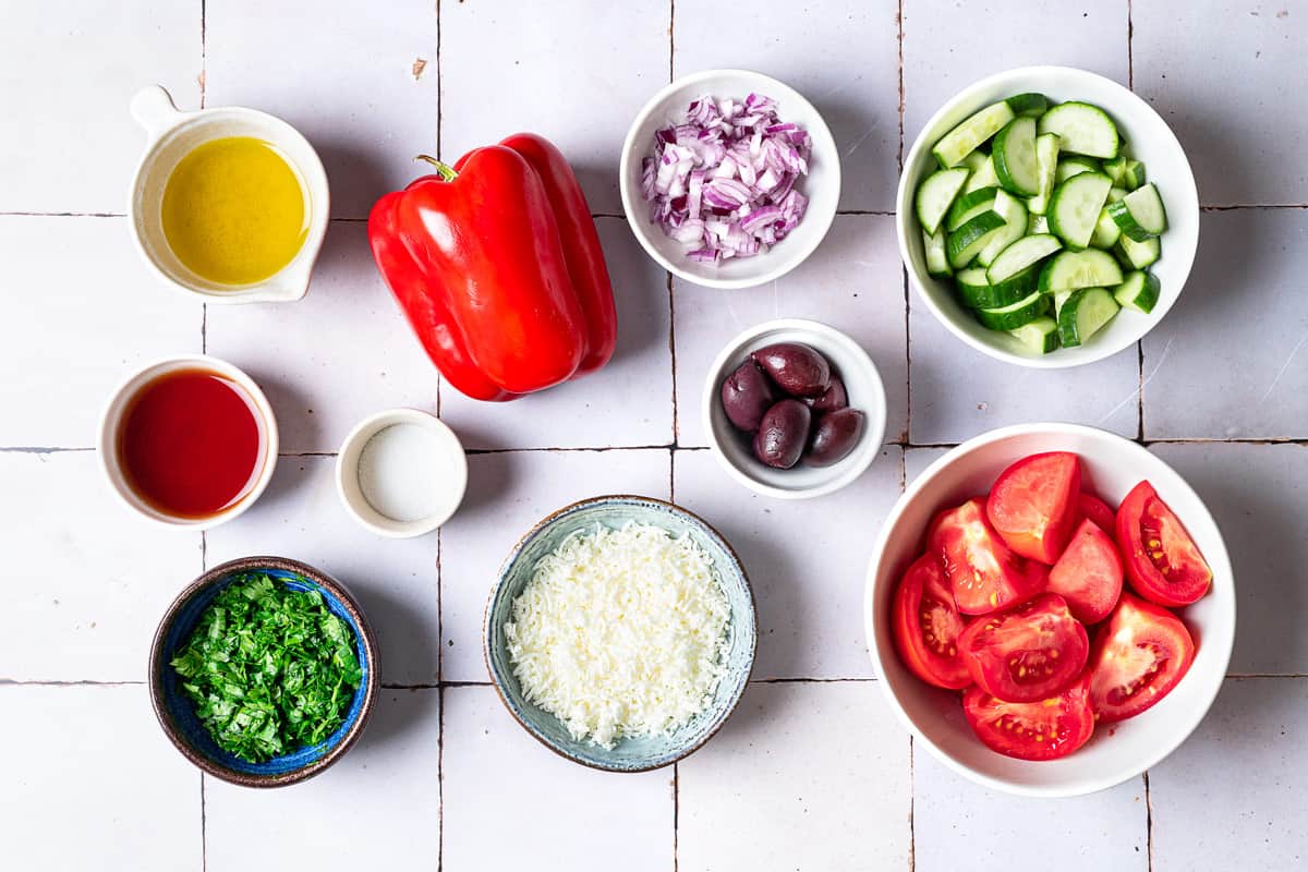 Ingredients for Shopska Salad, including cucumbers, tomatoes, white cheese, parsley, olives, olive oil, salt, red pepper, and vinegar.