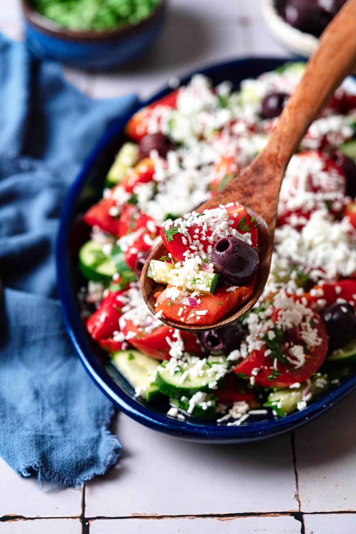 close up shot of a spoonful of shopska salad in a wooden serving spoon with a large platter in the background.