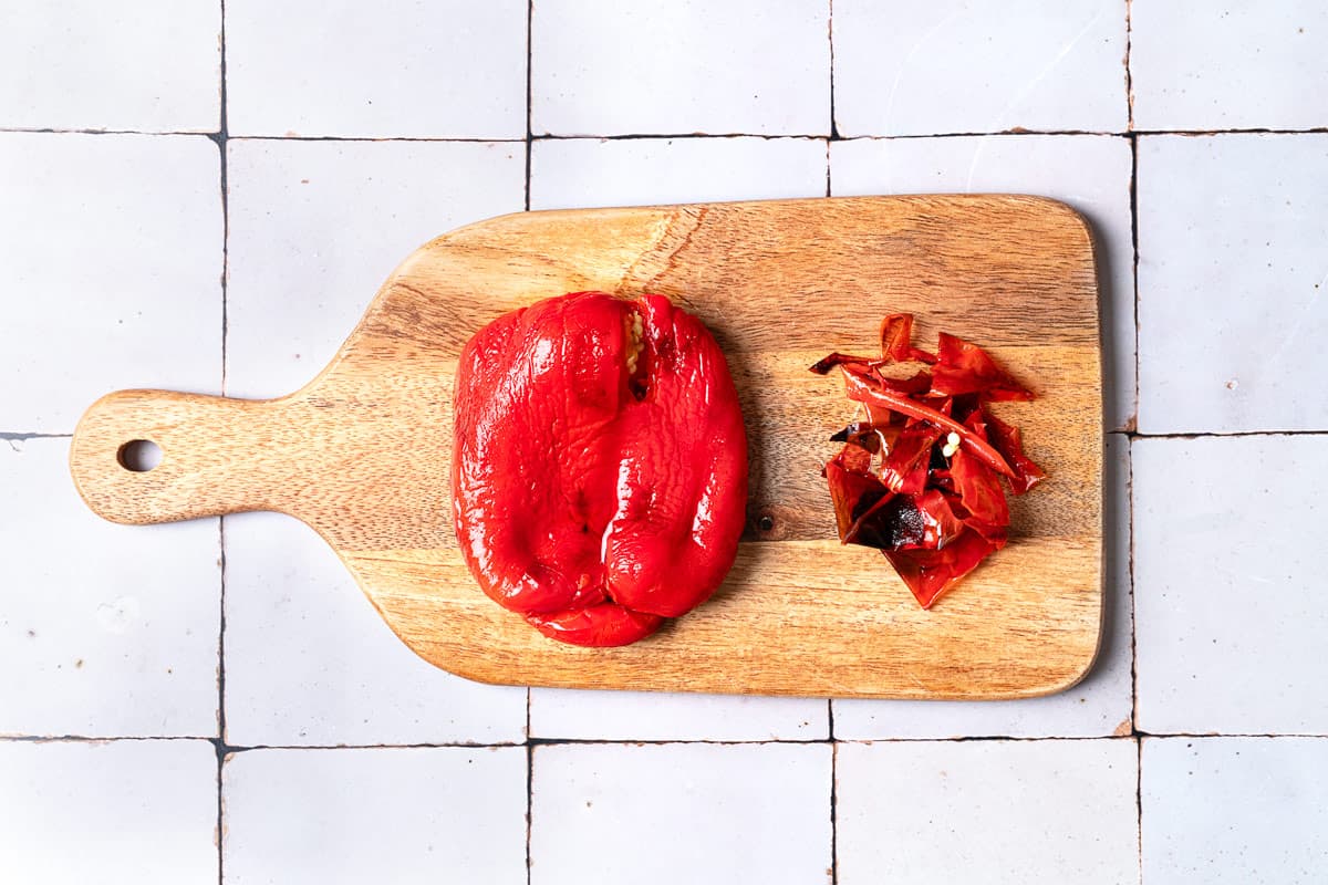 One roasted red pepper on a cutting board with its skin peeled off.