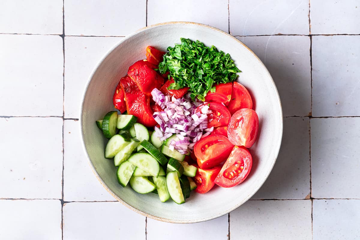 Tomatoes, onions, cucumbers, roasted red peppers, and shallot in a mixing bowl.