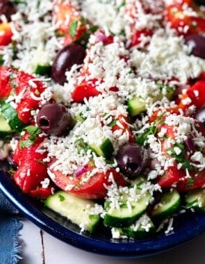 Close up shot of shopska salad with tomatoes, herbs, olives, and grated cheese.