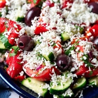 Close up shot of shopska salad with tomatoes, herbs, olives, and grated cheese.