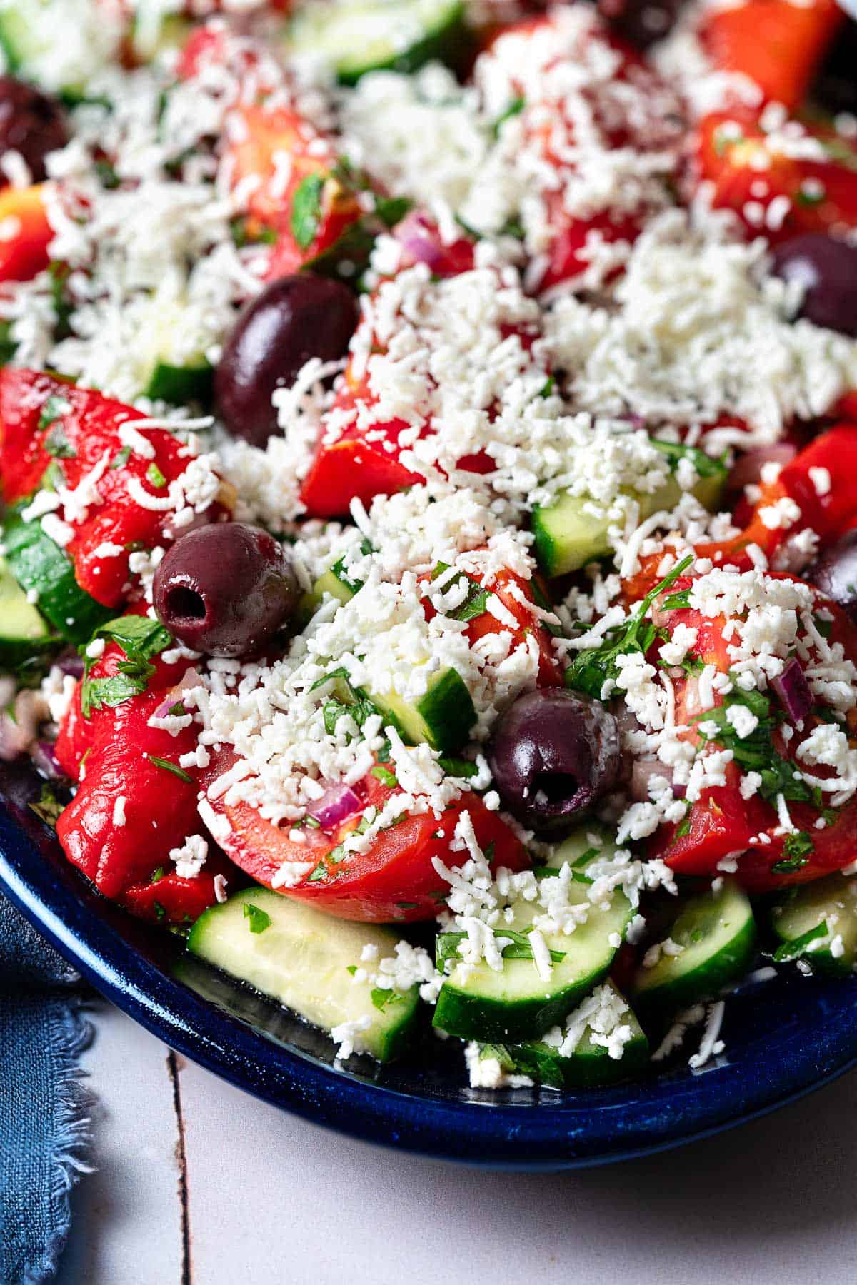 Close up shot of shopska salad with tomatoes, herbs, olives, and grated cheese.