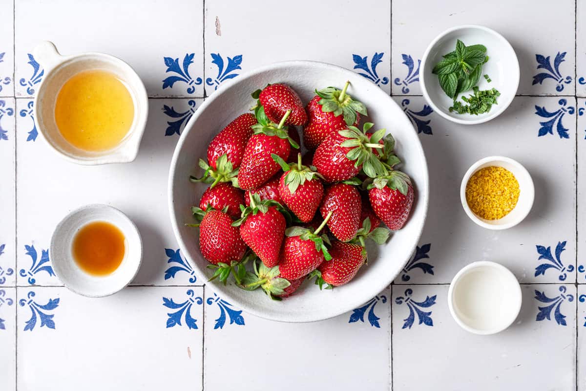 ingredients for strawberry compote including strawberries, vanilla extract, rosewater, honey, lemon zest, and mint.