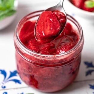 a spoonful of strawberry compote being lifted from a jar of strawberry compote.