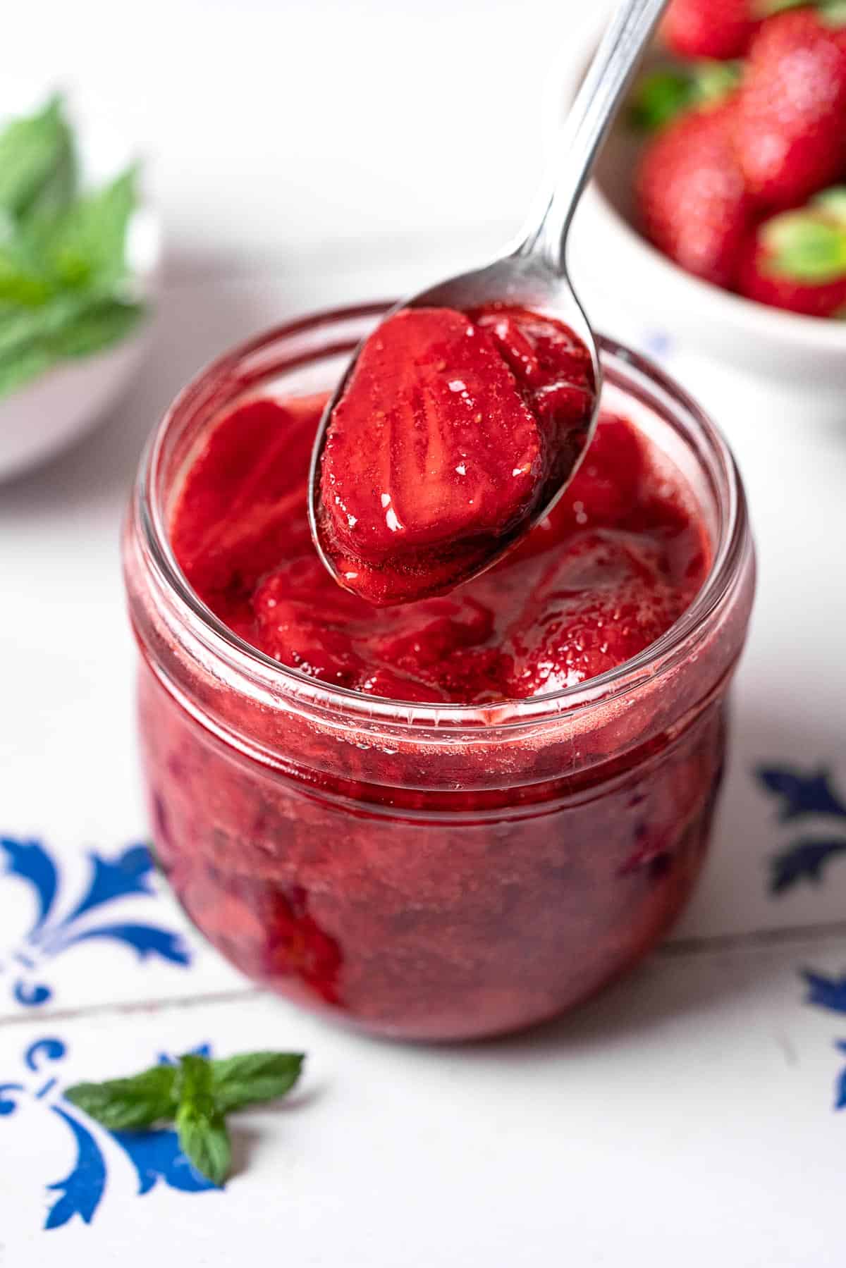 a spoonful of strawberry compote being lifted from a jar of strawberry compote.