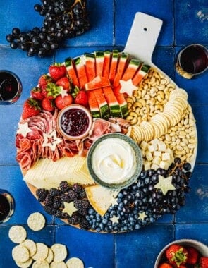 overhead photo of a complete fruit charcuterie board surrounded by 3 glasses of wine, grapes, a bowl of strawberries, and a group of crackers.