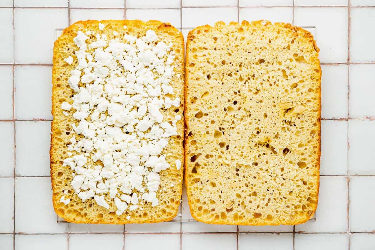 a focaccia loaf sliced in half with cheese sprinkled on one side.