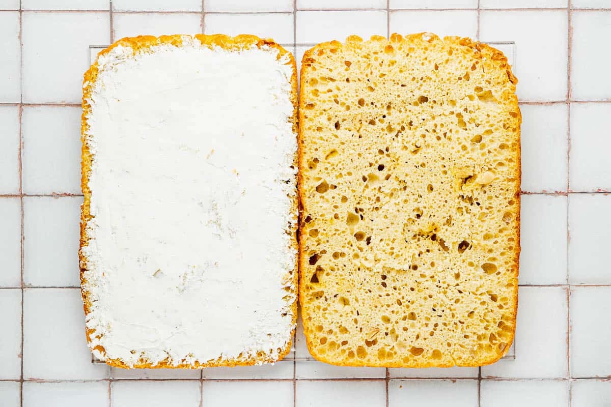 a focaccia loaf sliced in half with cheese spread on one side.