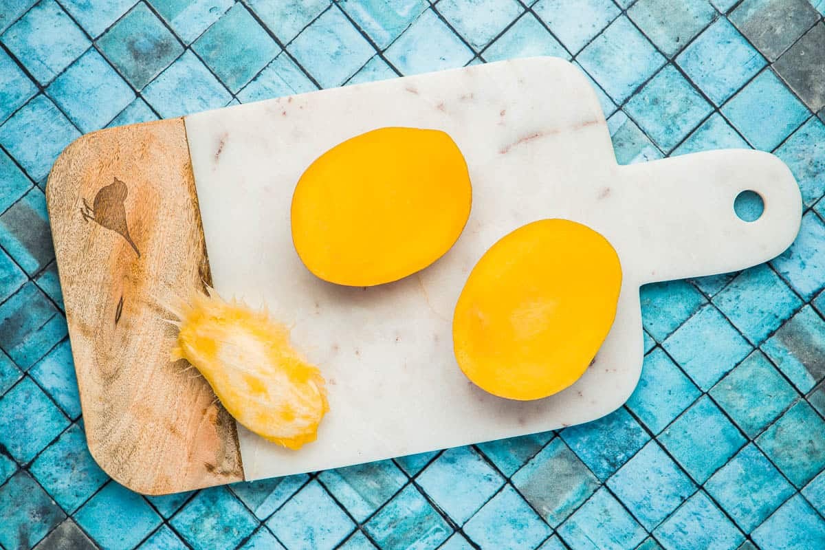 two mango halves and the mango seed on a cutting board.