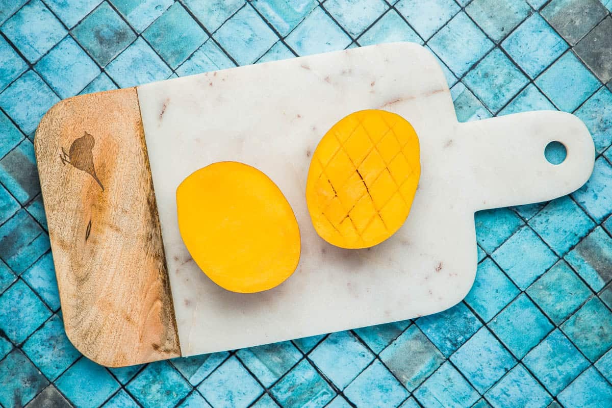 two mango halves on a cutting board, one scored.