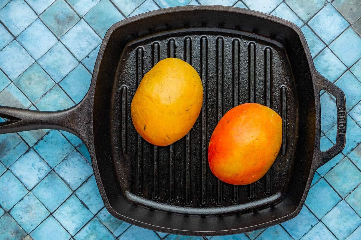 two mango halves on a cast iron grill pan.