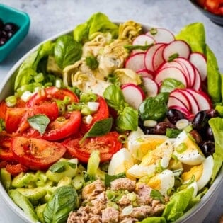 An entire nicoise salad in a serving bowl next to a bowl of artichoke hearts and a bowl of sliced tomatoes.