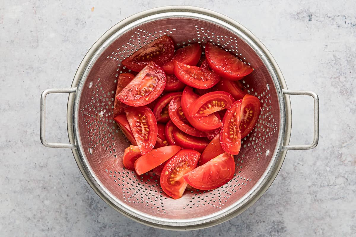 sliced tomatoes sprinkled with salt in a colander.