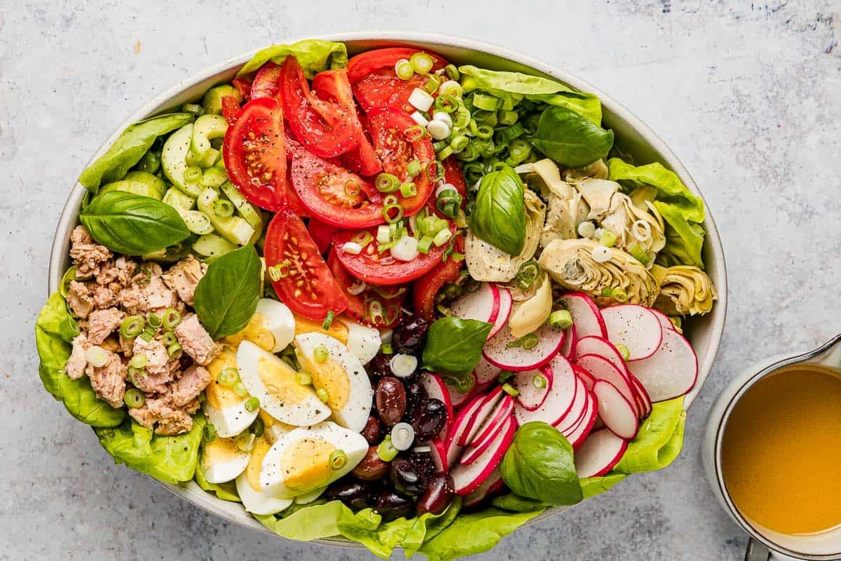 An entire nicoise salad in a serving bowl next to a bowl of dressing.