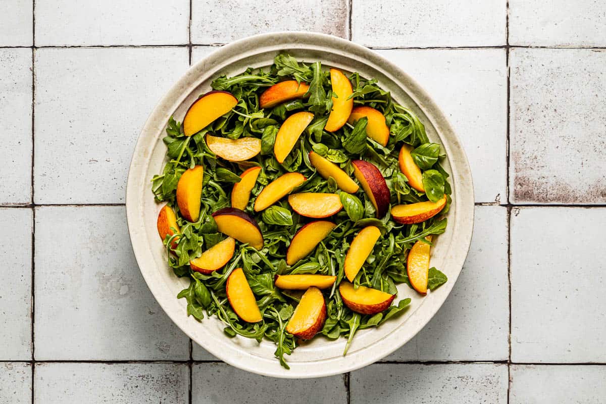 sliced peaches layered on arugula in a serving bowl.