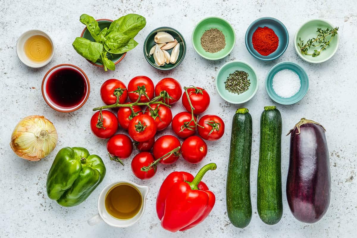 ingredients for ratatouille including eggplant, salt, pepper, olive oil, onion, bell peppers, tomatoes, garlic, zucchini, red wine, thyme, paprika, rosemary, sherry vinegar, and basil.