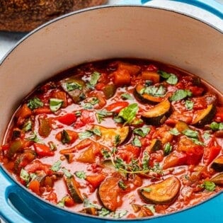 cooked ratatouille in a pot next to a round loaf of bread.