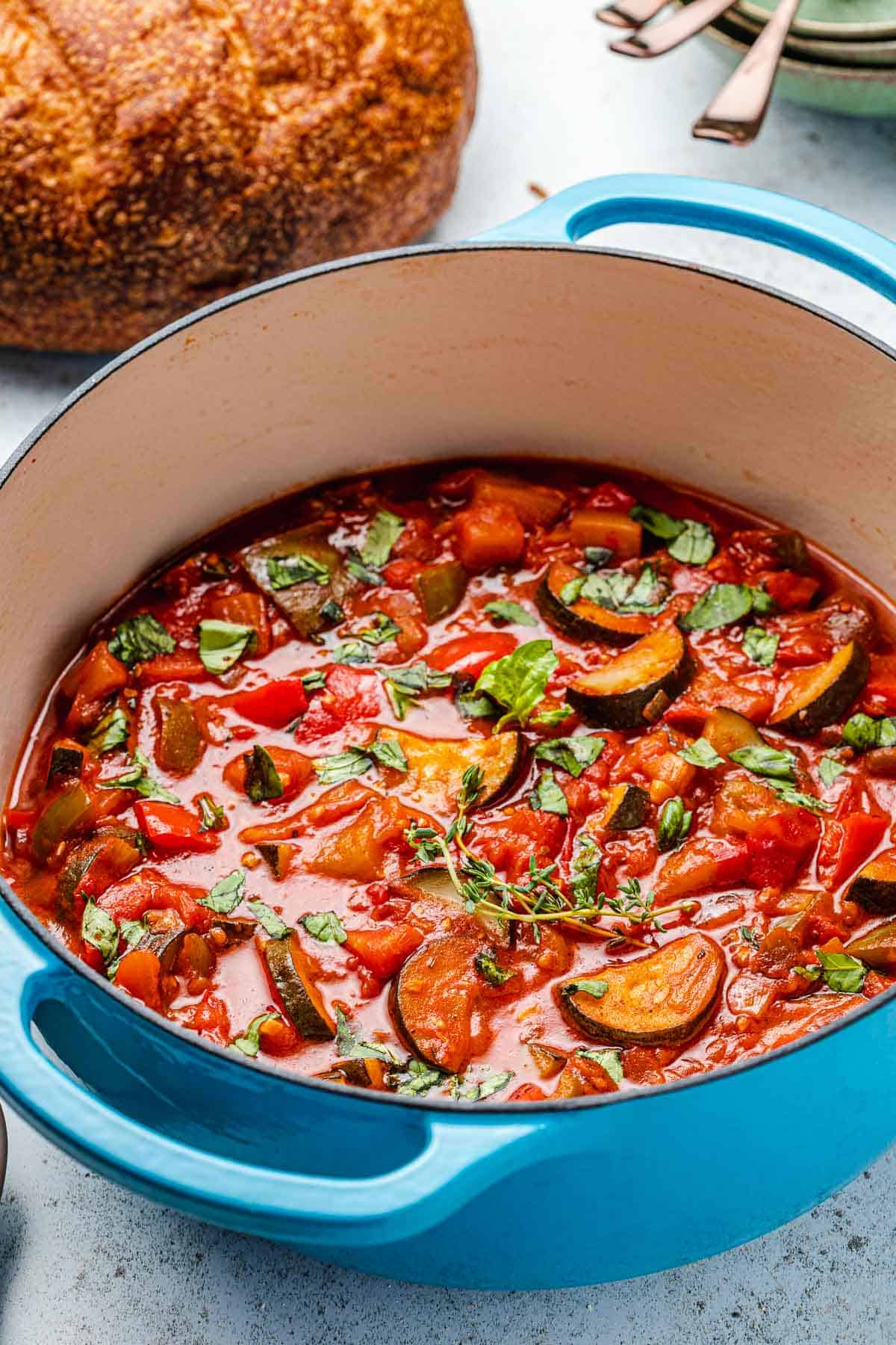 cooked ratatouille in a pot next to a round loaf of bread.