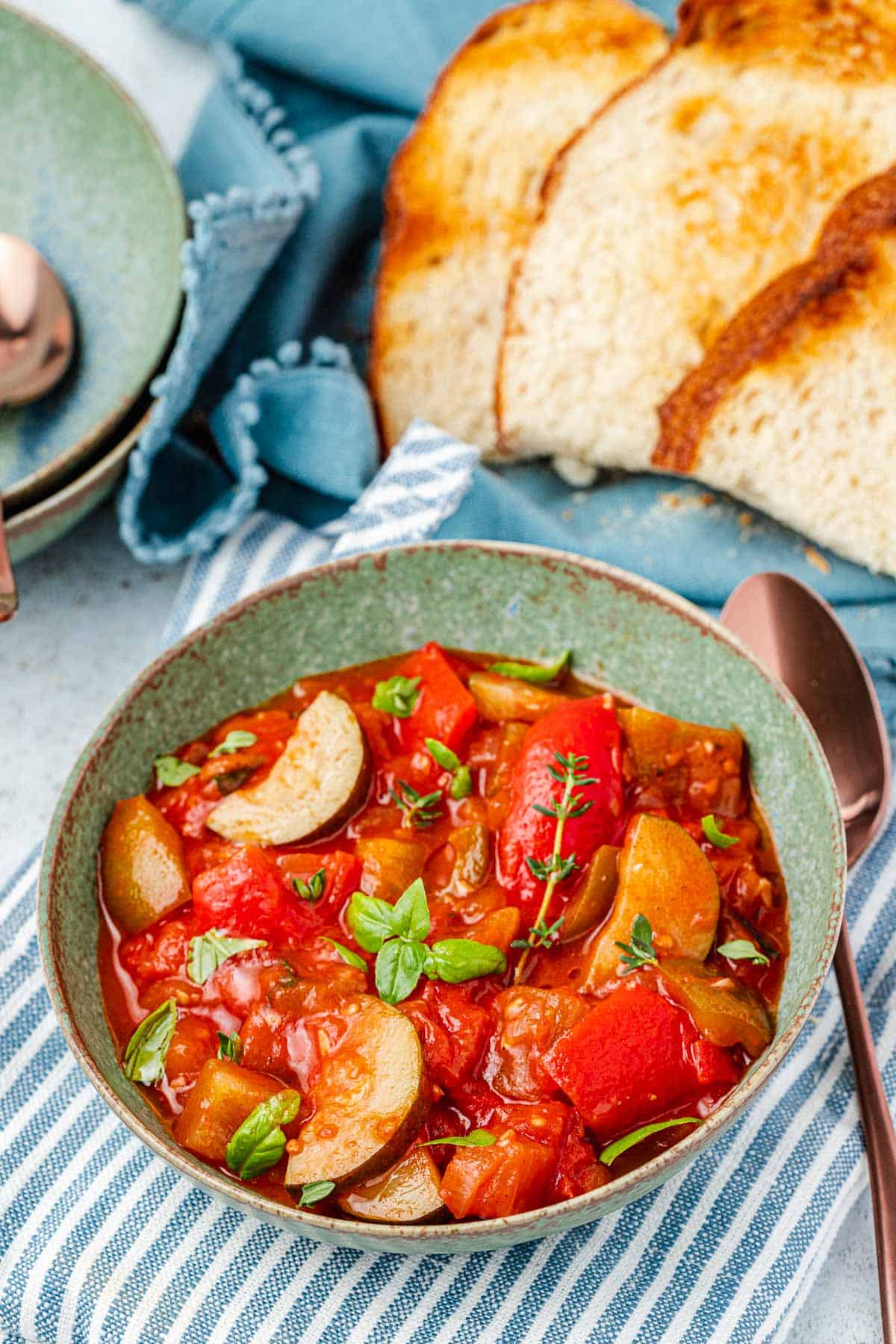 ratatouille in a bowl next to a spoon, and slices of toasted bread.