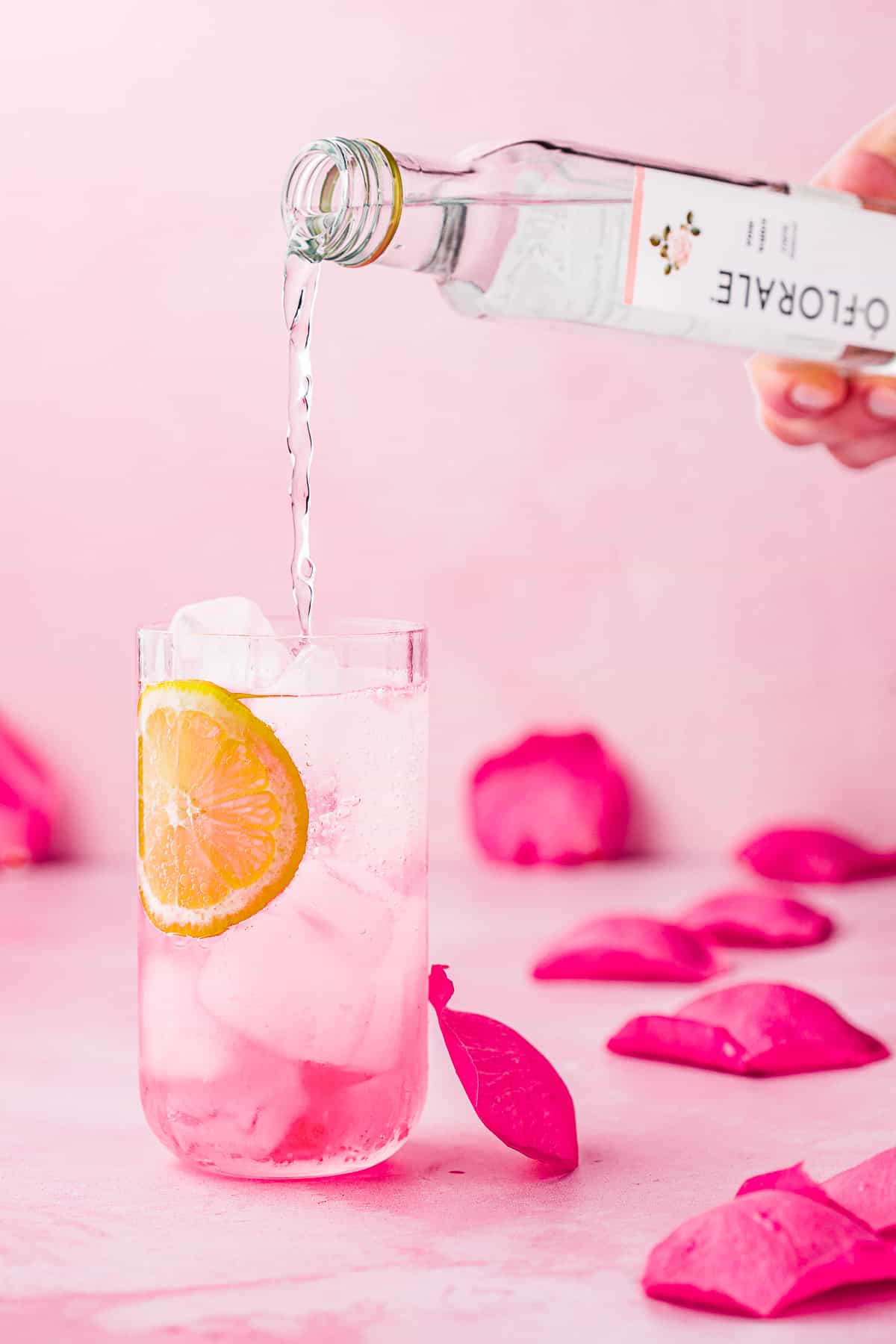rose water being poured into a glass with a garnish of sliced lemon.