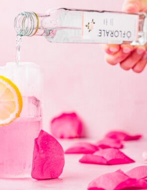 rose water being poured into a glass with a garnish of sliced lemon.