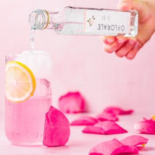 rose water being poured into a glass with a garnish of sliced lemon.
