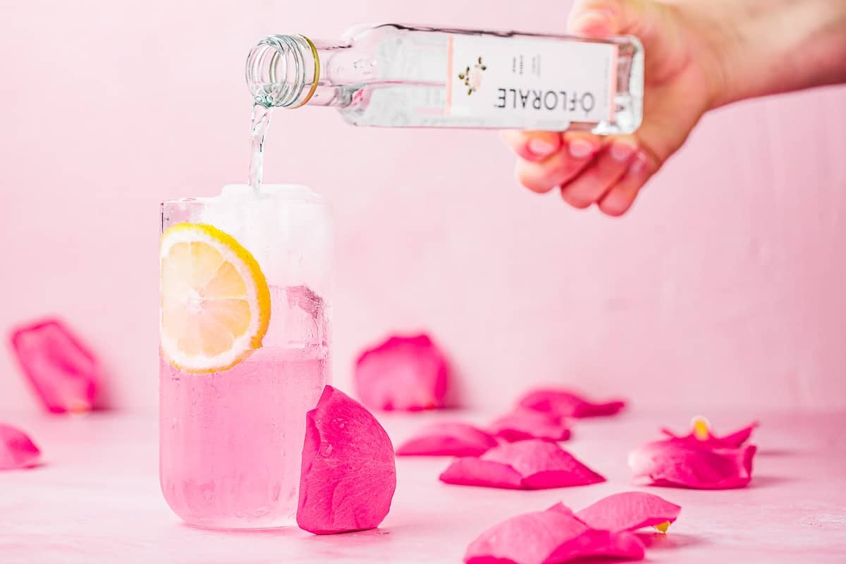 rose water being poured into a glass with a garnish of sliced lemon.