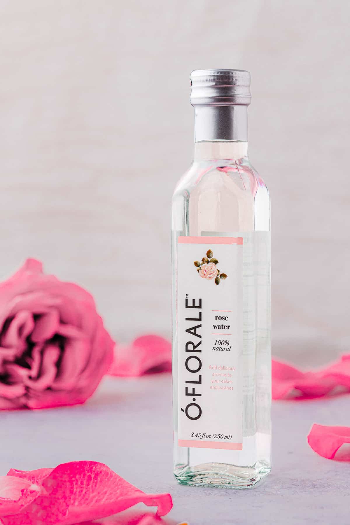 a bottle of o'florale rose water next to a pink rose and rose petals.