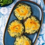 4 cooked stuffed portobello mushrooms on a serving platter next to a bowl of baby spinach.