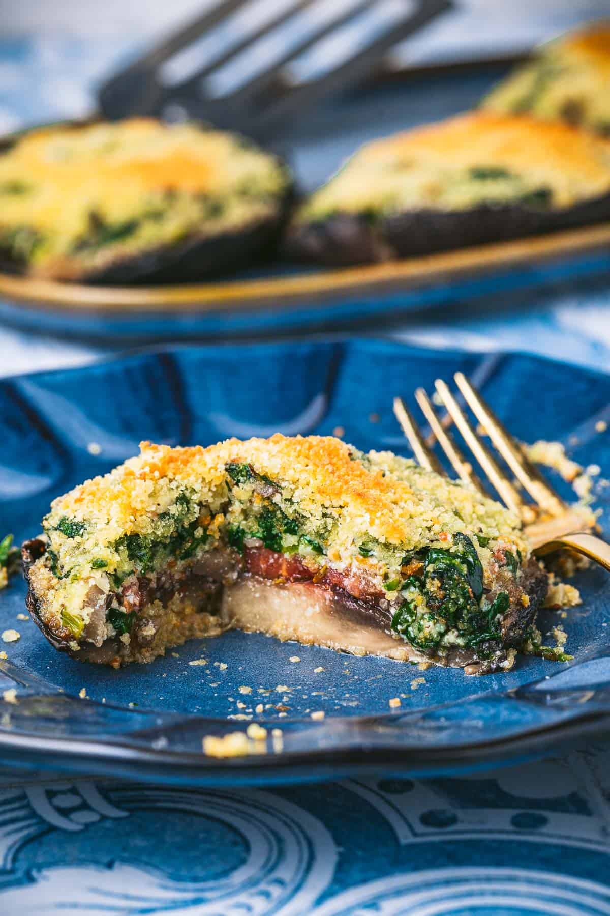 a cooked stuffed portobello mushroom on a plate with a fork.