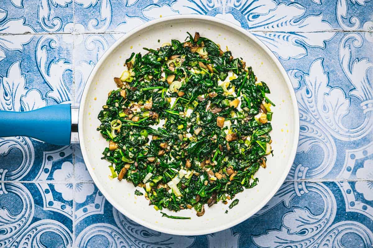 sauteed chopped mushroom stems, garlic, spinach, and green onion in a skillet.