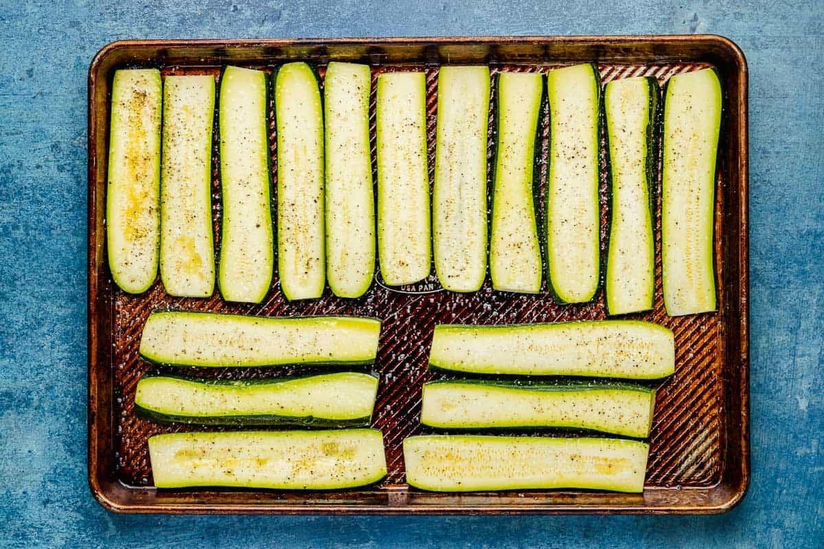 long, unbaked slices of zucchini on an oiled baking sheet, seasoned with salt and pepper.