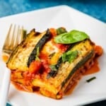 a slice of zucchini parmesan topped with basil leaves on a plate with a fork.