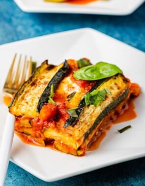 a slice of zucchini parmesan topped with basil leaves on a plate with a fork.