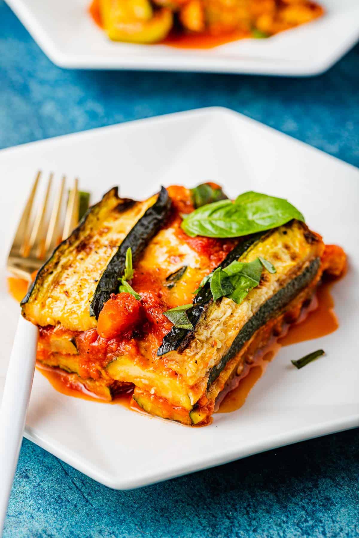 a slice of zucchini parmesan topped with basil leaves on a plate with a fork.