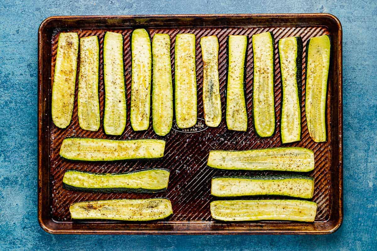 long, baked slices of zucchini on an oiled baking sheet, seasoned with salt and pepper.