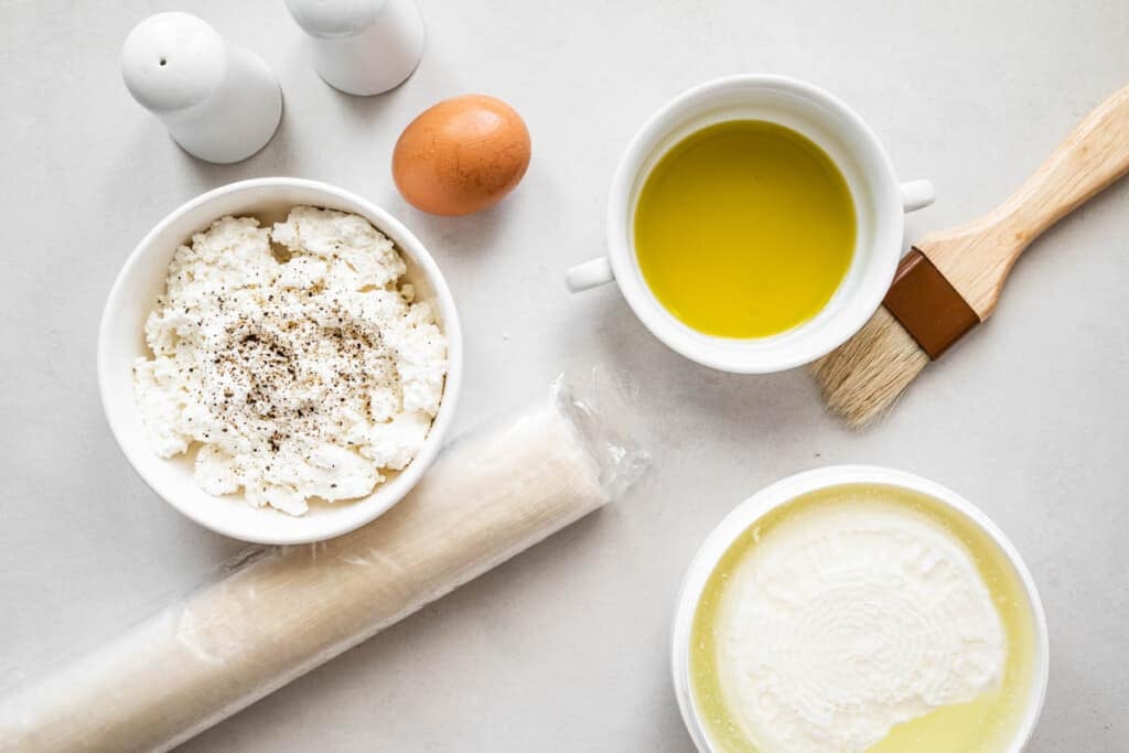 ingredients for tiropitakia feta hand pies including filo dough, feta cheese, and egg, olive oil, and ricotta cheese.