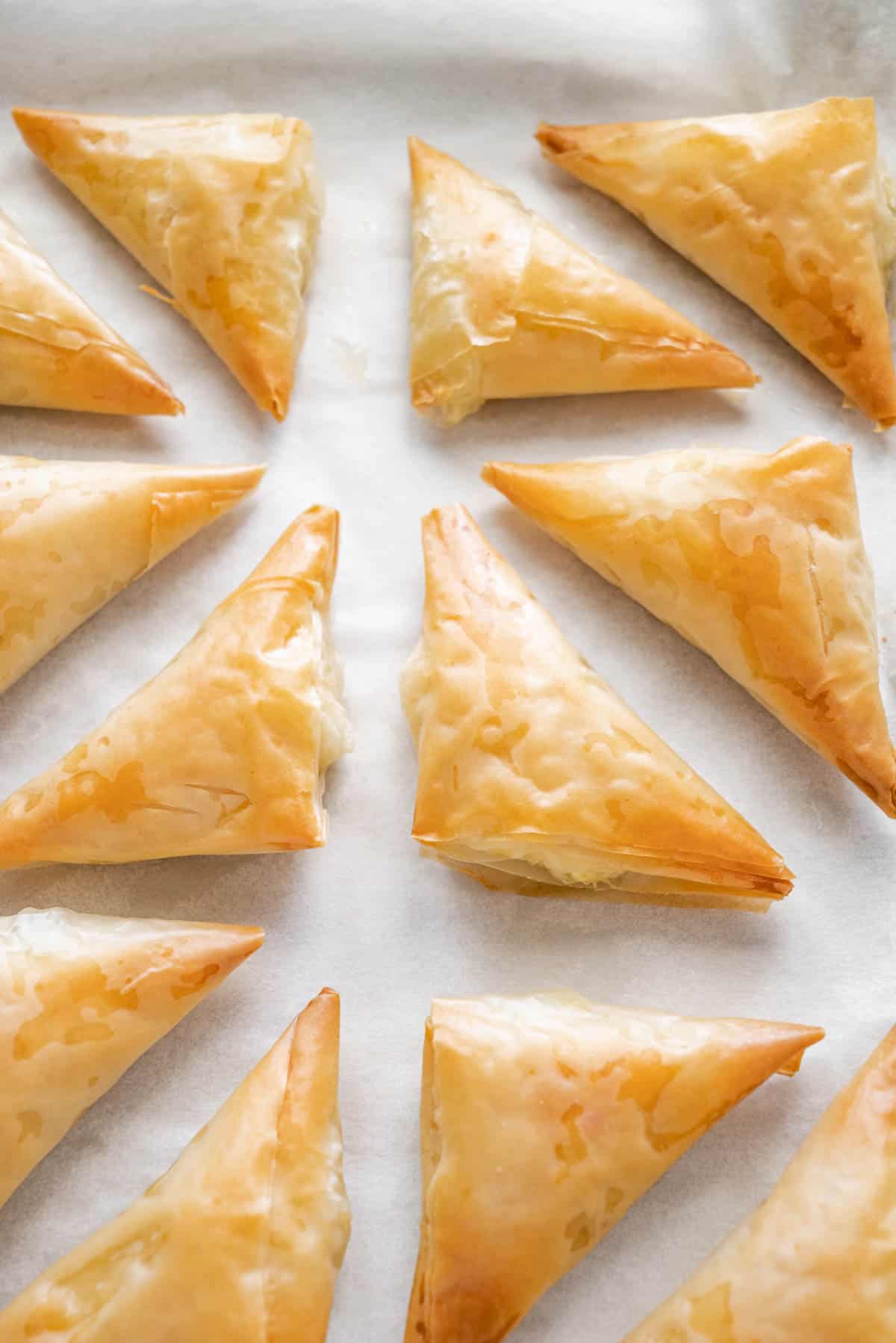several baked, triangle-shaped tiropitakia feta hand pies on parchment paper.