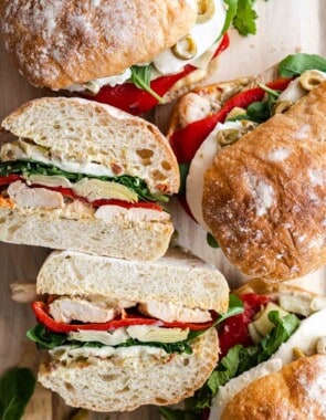 four antipasto chicken sandwiches on a serving board, one cut in halve showing it's ingredients.