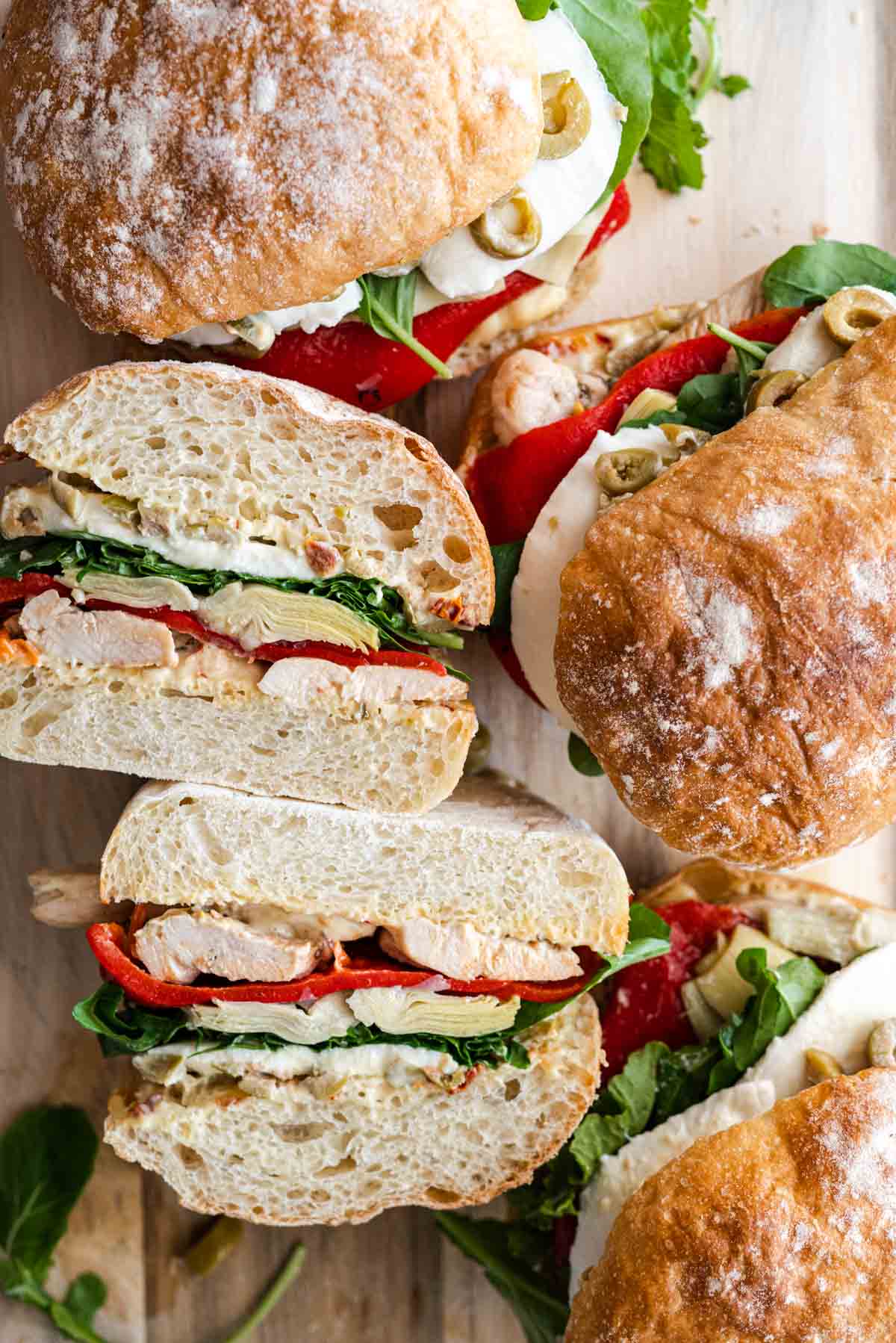 four antipasto chicken sandwiches on a serving board, one cut in halve showing it's ingredients.