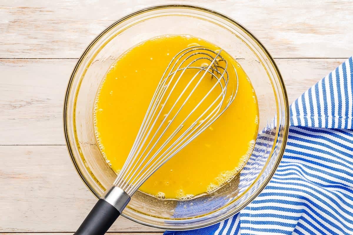 wet ingredients for blueberry muffins mixed together in a bowl with a whisk.