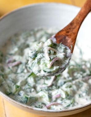 a bite of creamy cucumber salad being lifted out of a serving bowl with a wooden serving spoon.