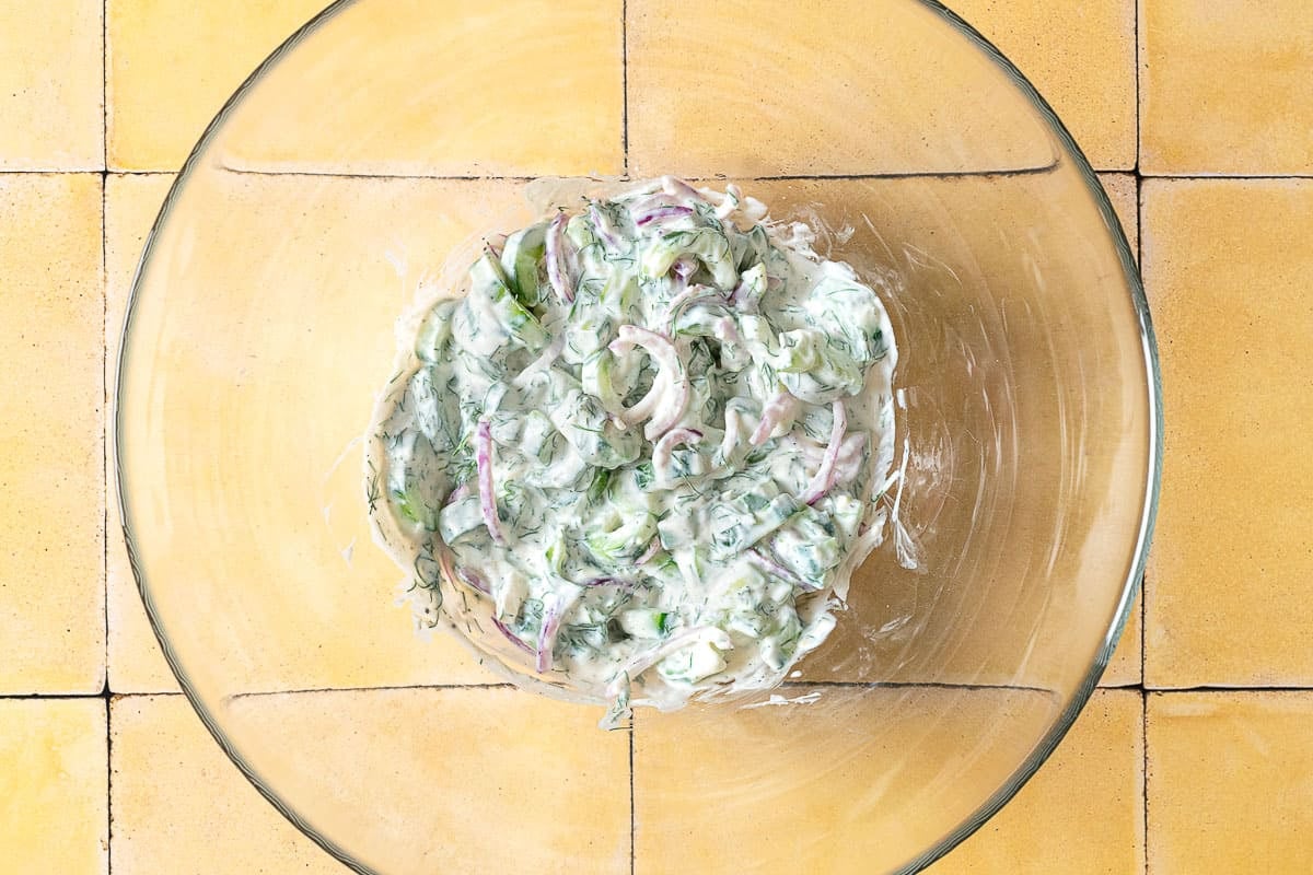 a creamy cucumber salad in a mixing bowl.