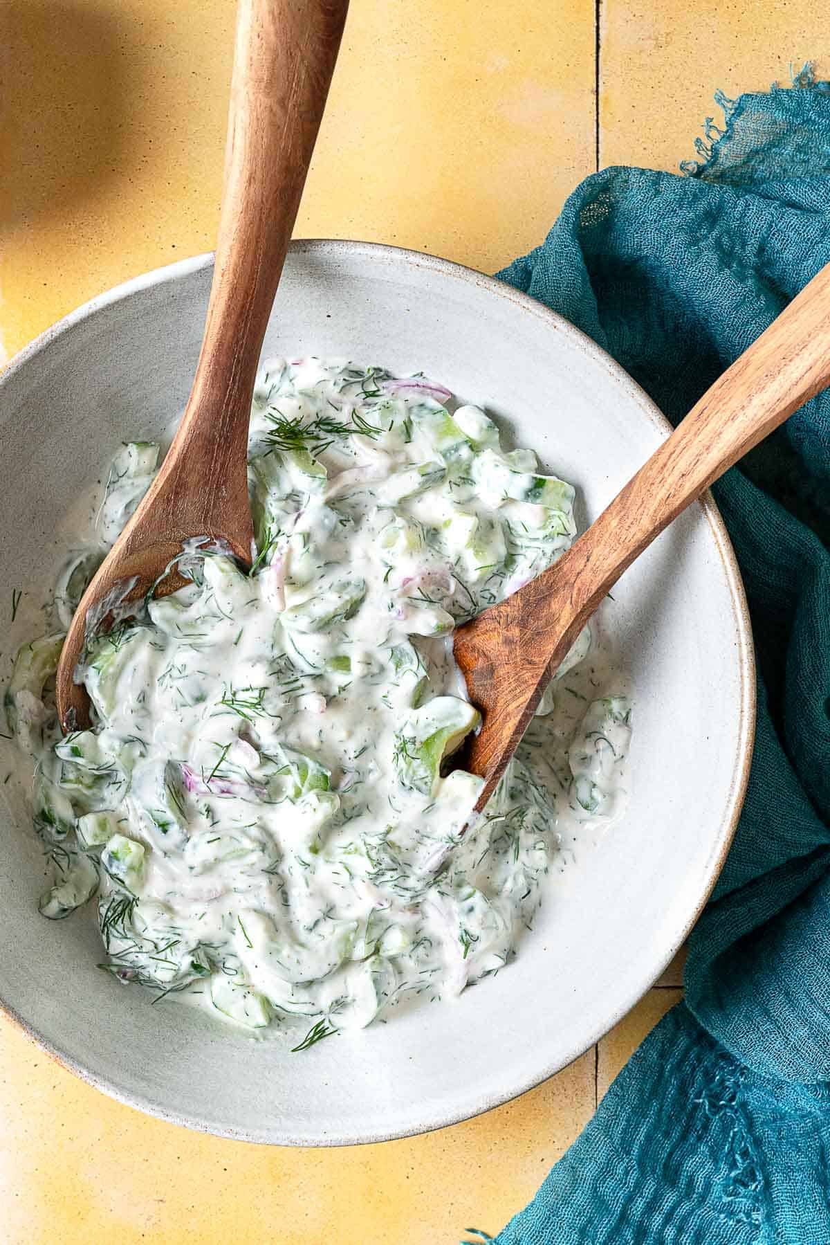 a creamy cucumber salad in a serving bowl with wooden serving utensils.
