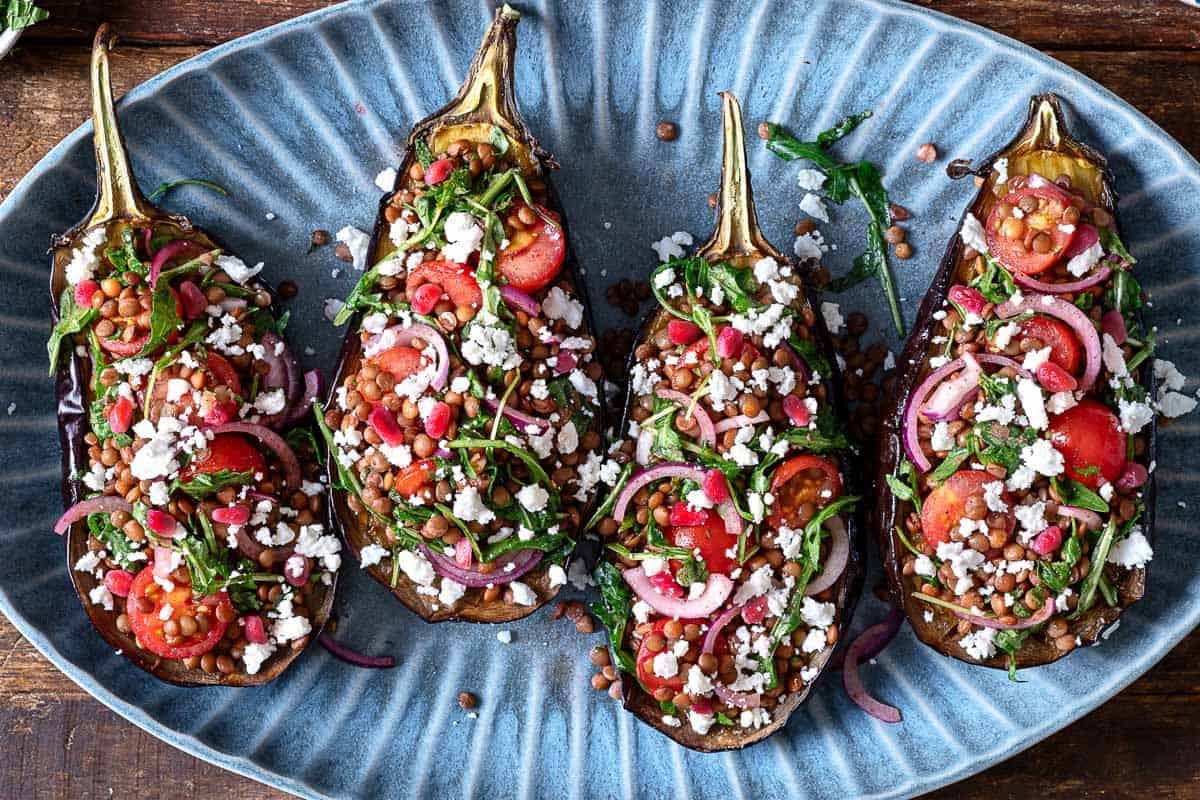 Overhead shot of eggplant salad, with eggplants stuffed with lentils, cherry tomatoes, arugula, and feta cheese and finished with a pomegranate dressing.