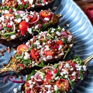 Eggplant salad with four eggplant halves stuffed with lentils, fresh vegetables, arugula, and feta cheese.