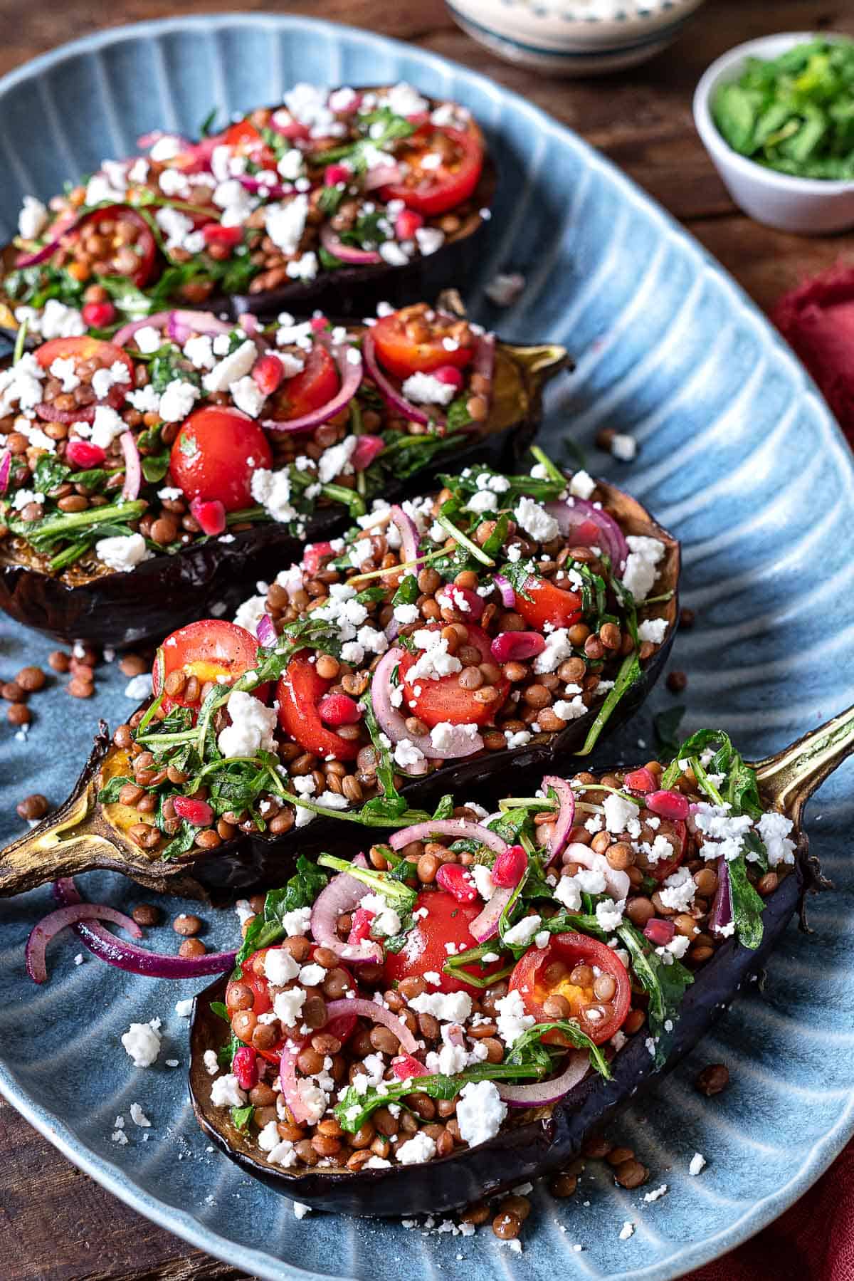 Eggplant salad with four eggplant halves stuffed with lentils, fresh vegetables, arugula, and feta cheese.