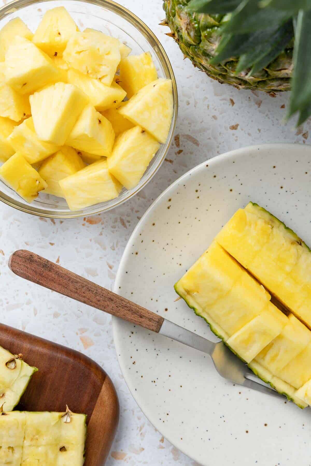 Sliced pineapple in a bowl with more sliced pineapple in a glass bowl on the side.