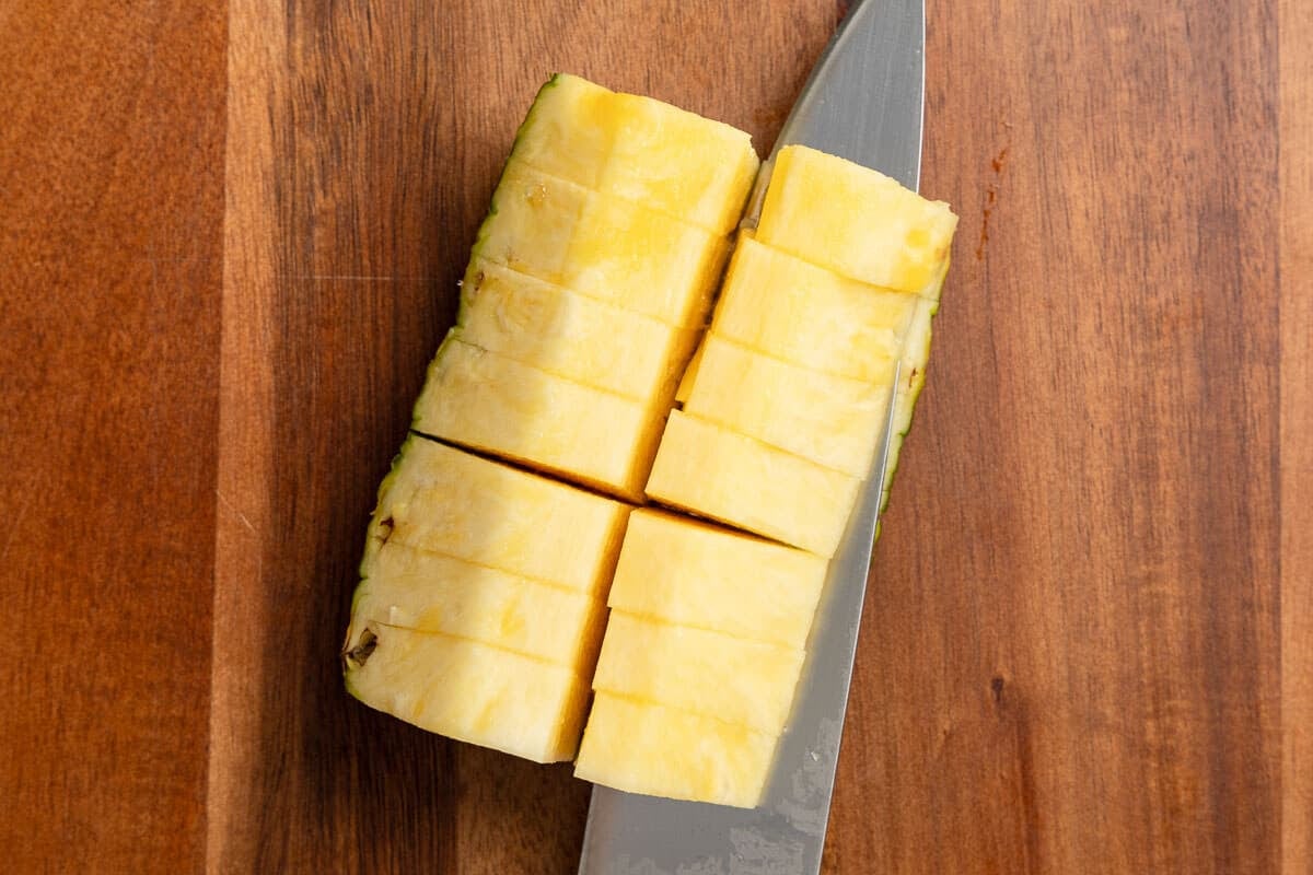 Knife removing the skin from the pineapple chunks.